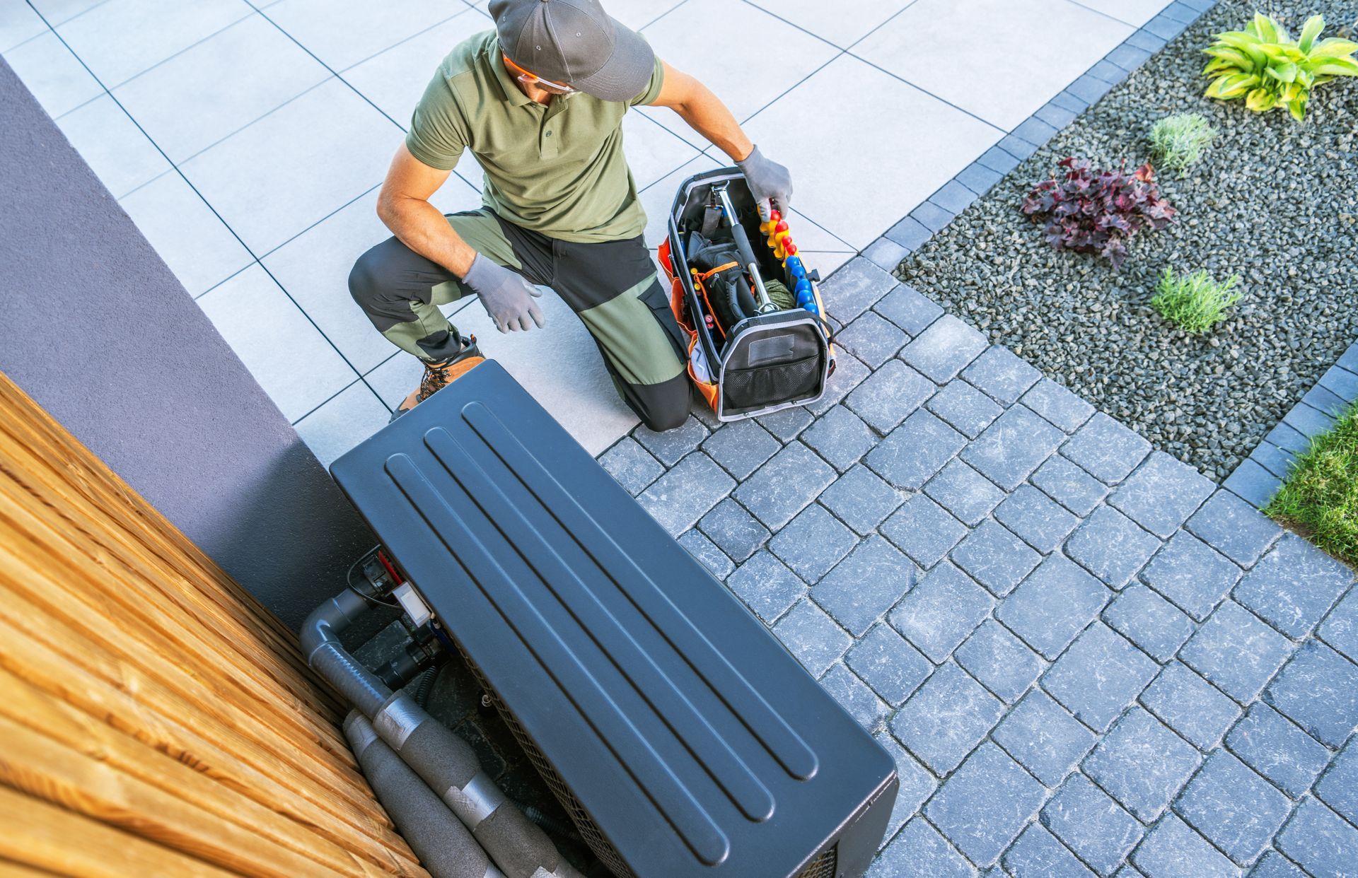 Worker handling a black machine beside a driveway and garden path, viewed from above Worker handling a black machine beside a driveway and garden path, viewed from above