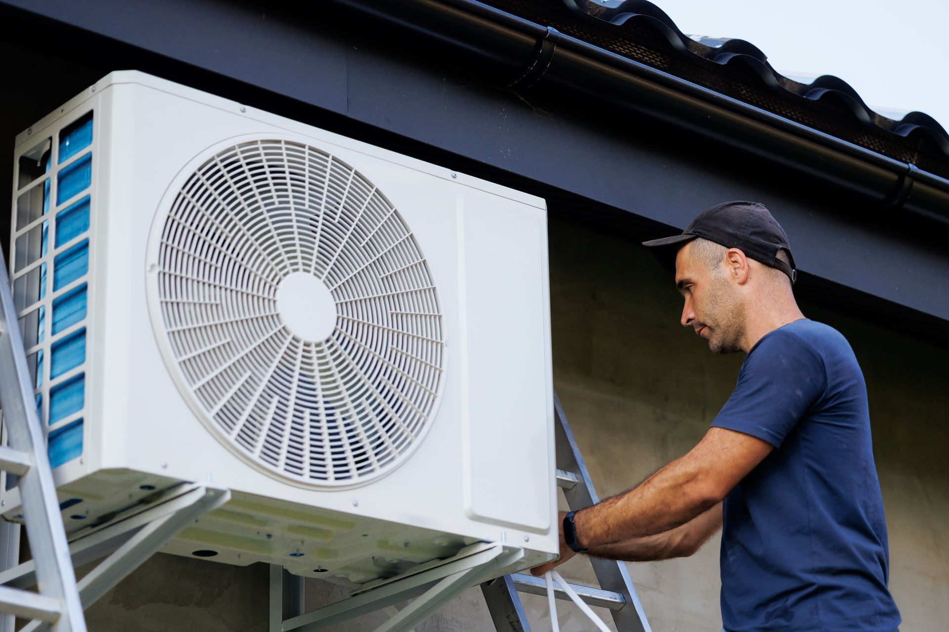 Technician servicing an outdoor air conditioner unit beside a house roof