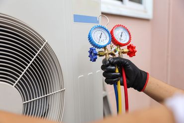 Hand holding HVAC manifold gauges beside an outdoor air conditioner unit Hand holding HVAC manifold gauges beside an outdoor air conditioner unit