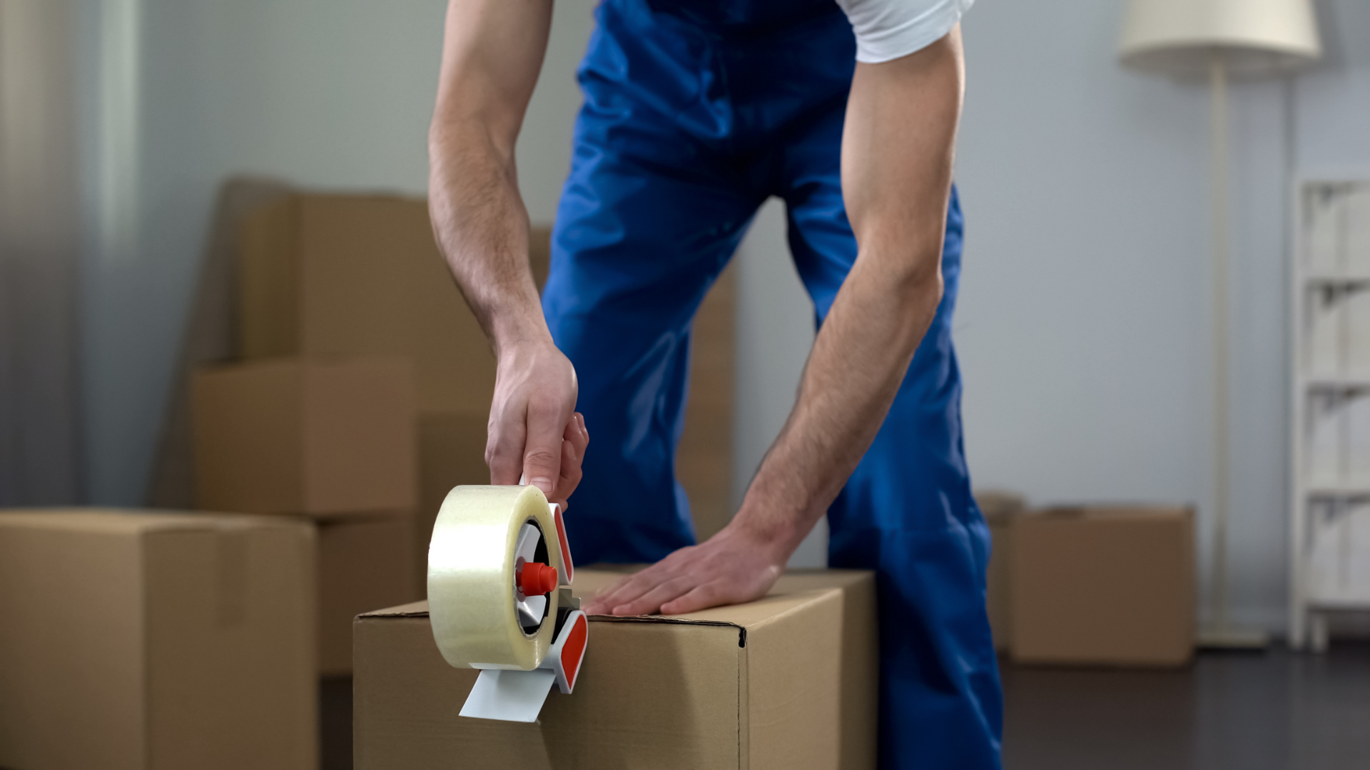 Person in blue overalls sealing a cardboard box with tape.
