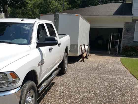 A white truck is parked in front of a house with a trailer attached to it.