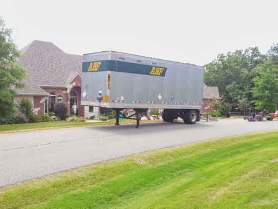 A large moving truck is parked on the side of the road in front of a house.