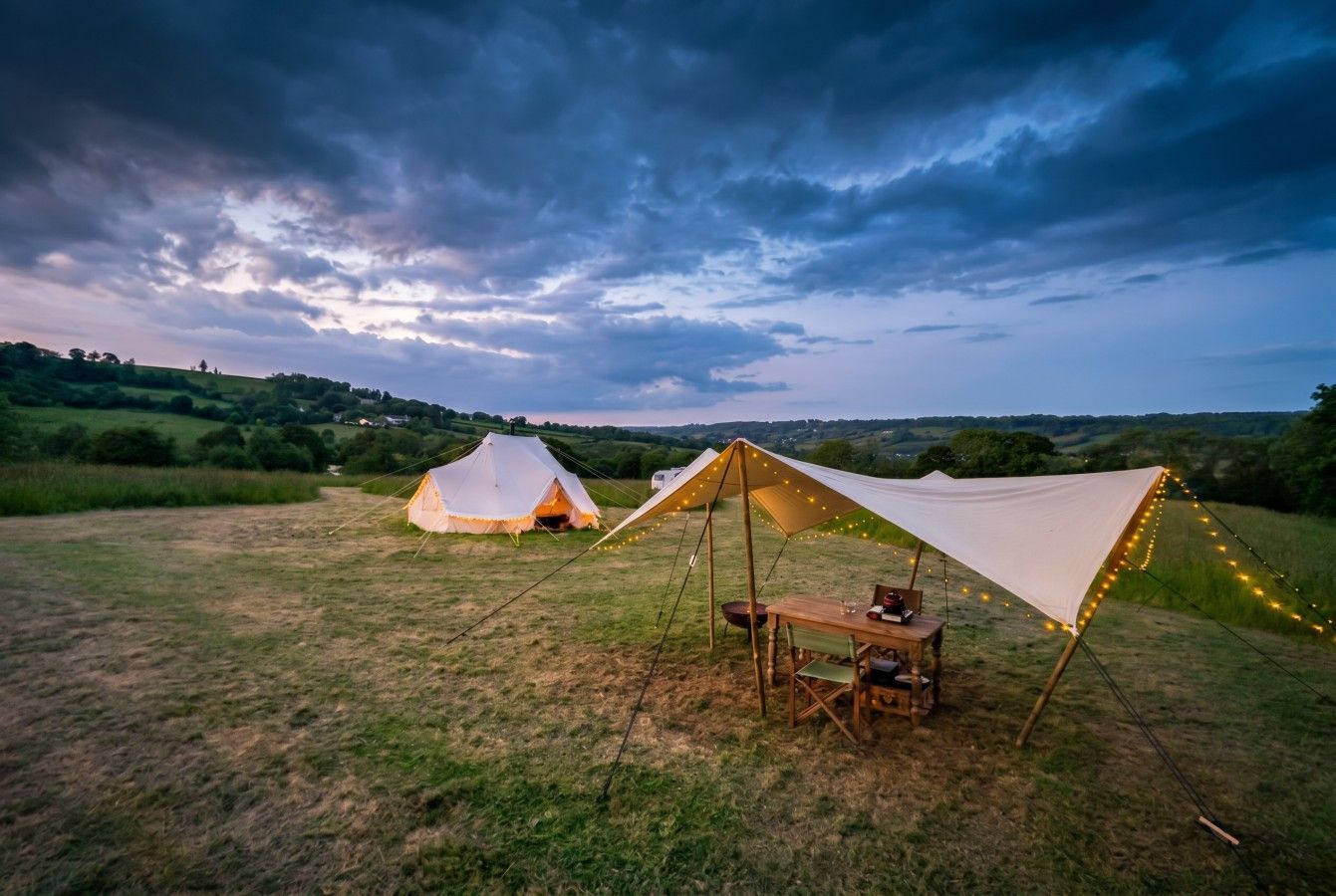 Camping tents on a grassy field at dusk under a dramatic cloudy sky