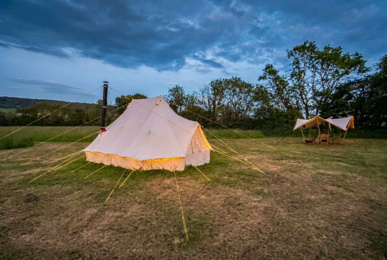 Two white tents on a grassy field at dusk under a cloudy sky