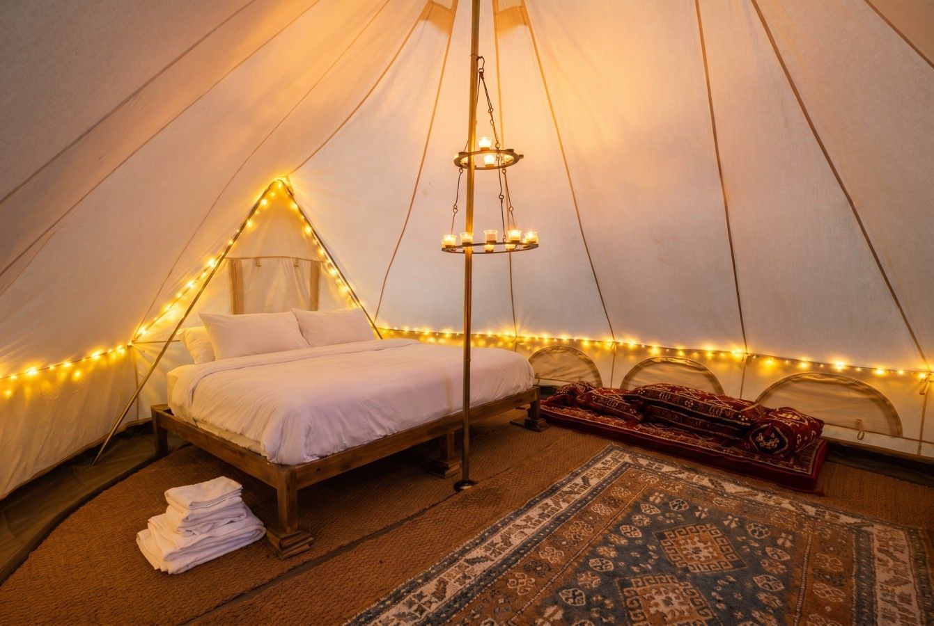 Cozy glamping tent with bed, string lights, rugs, and a warm boho interior