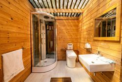 Wood-paneled bathroom with shower stall, toilet, sink, and towel rack under a corrugated ceiling