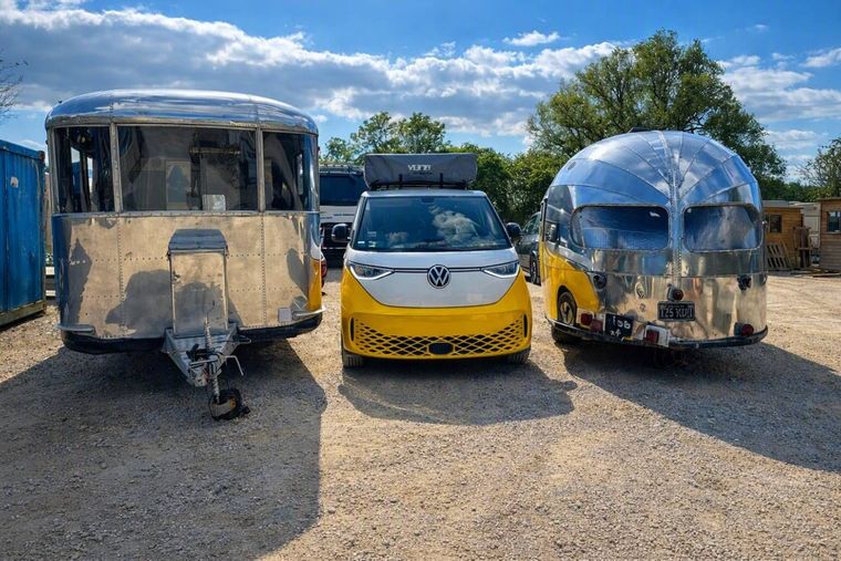 Three trailers and a white-and-yellow van parked on gravel under a partly cloudy sky.