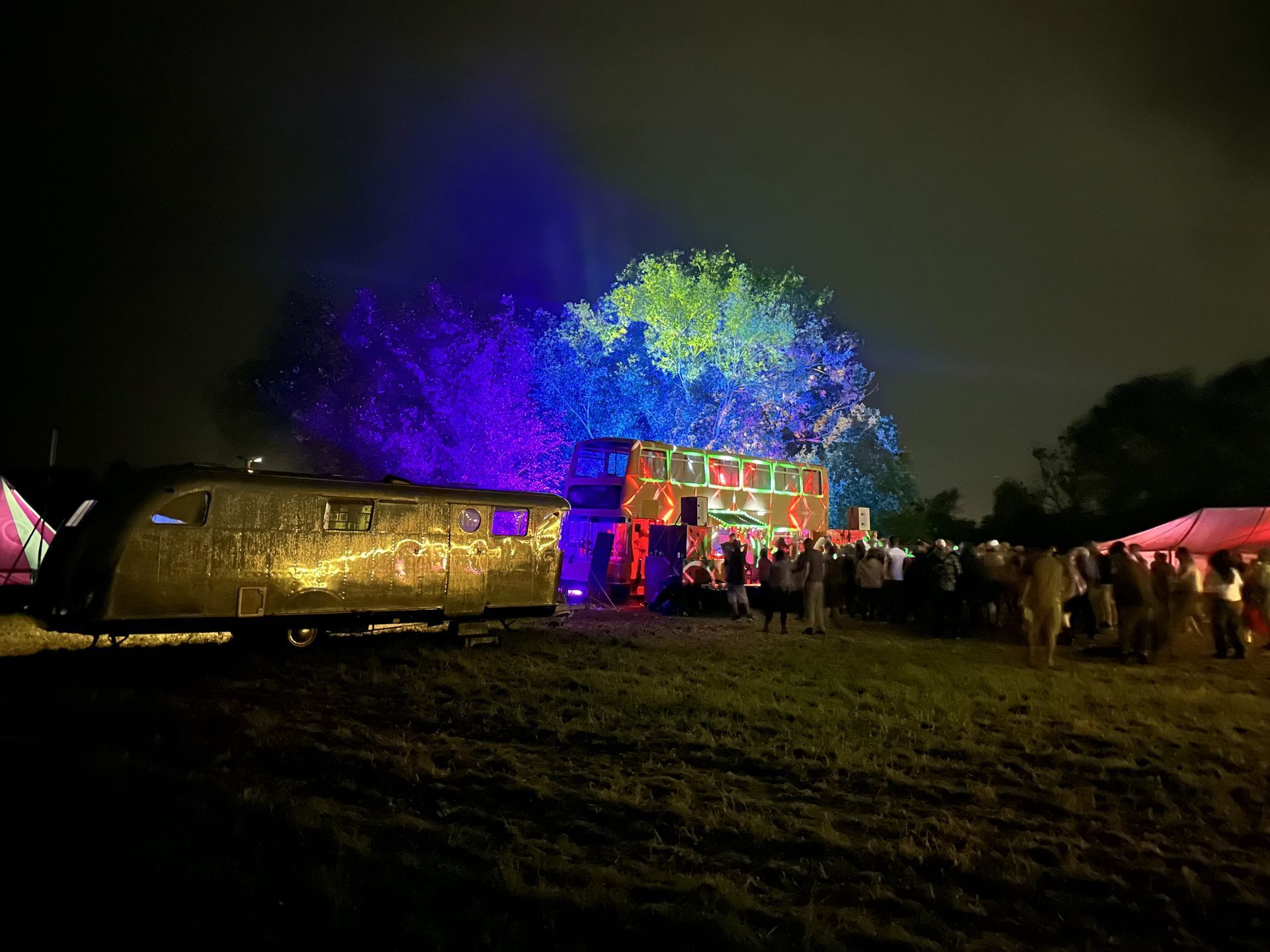 Nighttime festival scene with a brightly lit tree installation, a crowd, and a gold shuttle-like structure