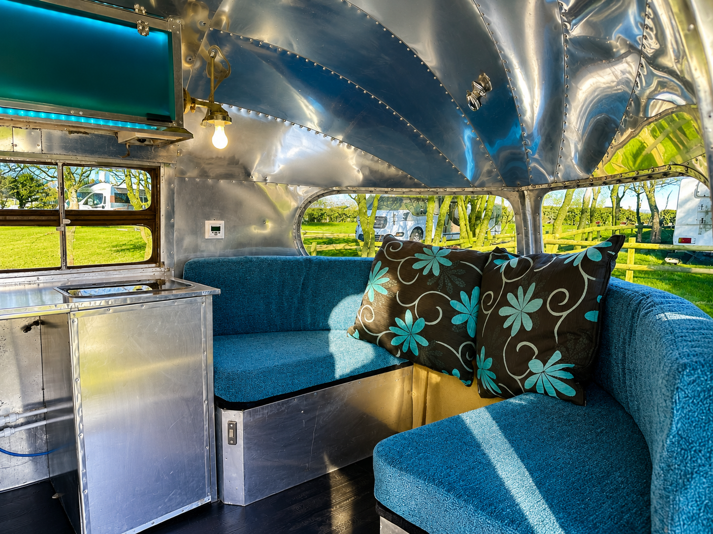 Blue vintage camper interior with curved metal ceiling, blue bench seats, and turquoise floral pillows