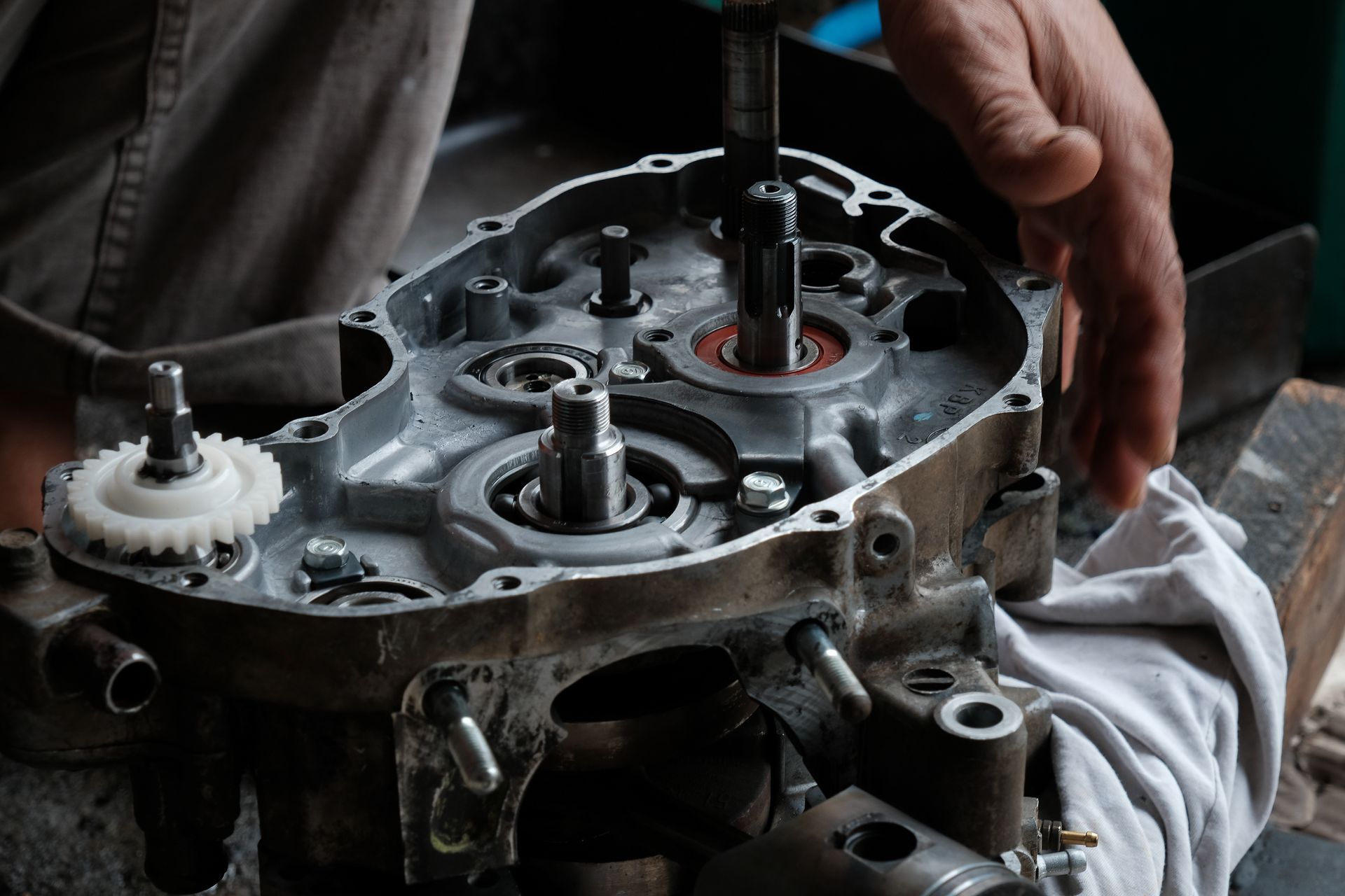 A mechanic's hands work on the exposed gears and shafts of an open engine crankcase.
