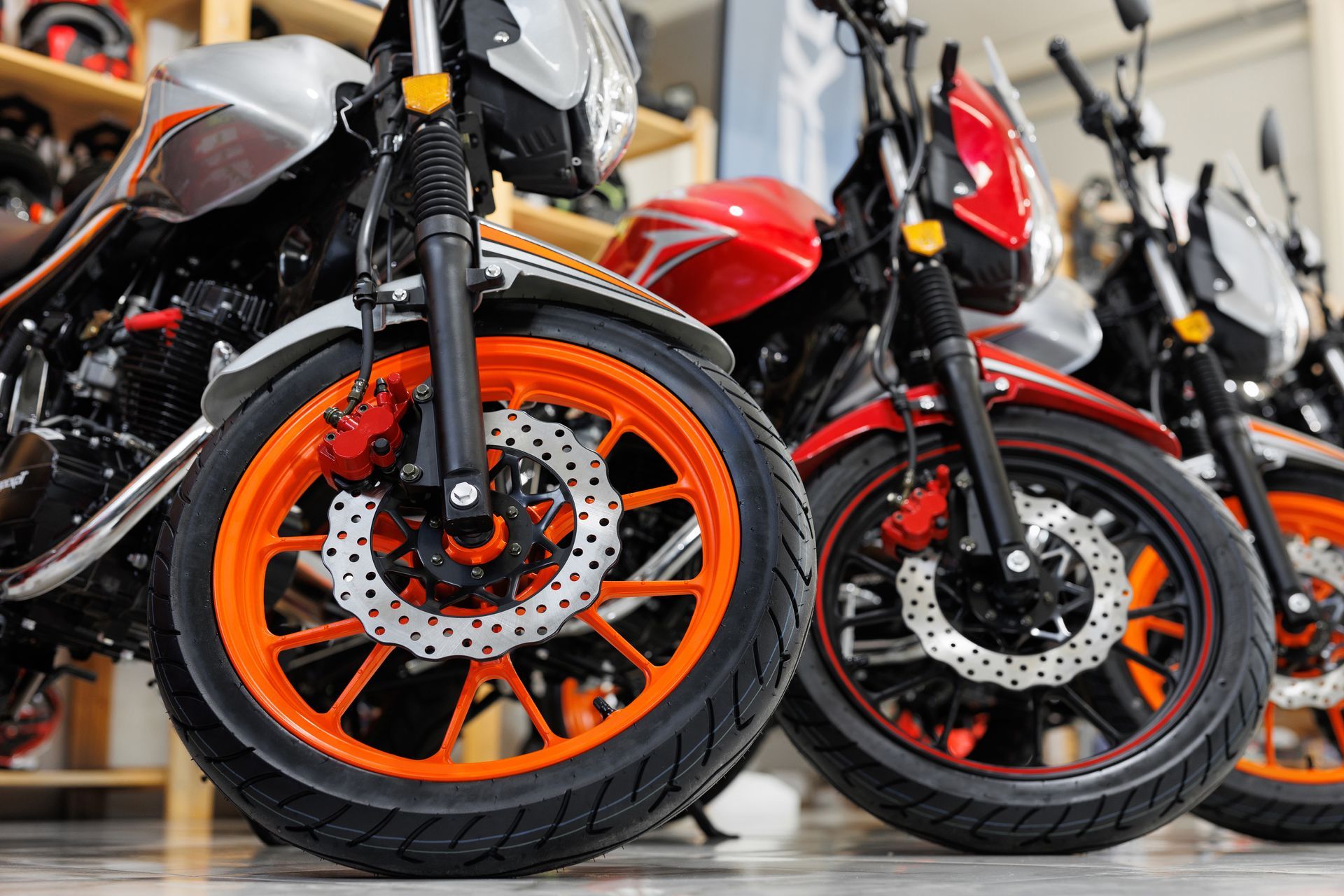 Close-up of three motorbikes with orange-rimmed wheels parked in a showroom.