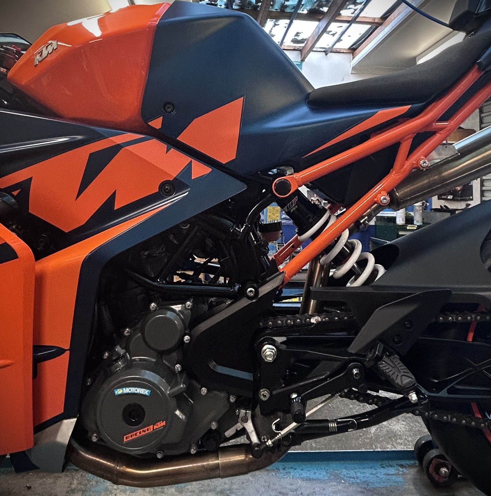 Orange-and-black KTM motorcycle close-up, showing the frame, engine, and seat indoors.