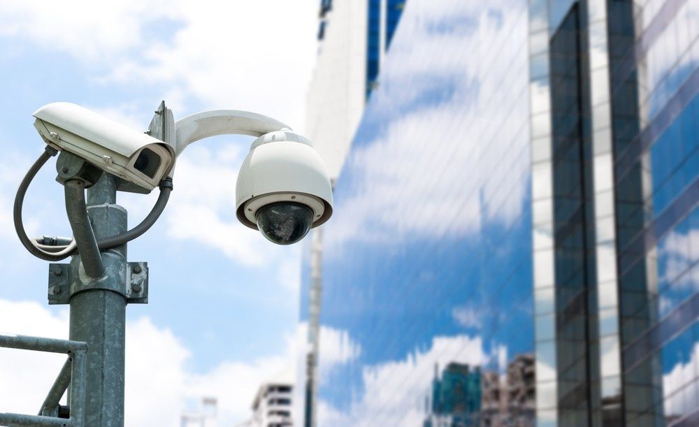 A Two Security Cameras on a Pole in Front of a Modern Glass Building — McGrath Electrical & Data in Port Macquarie, NSW