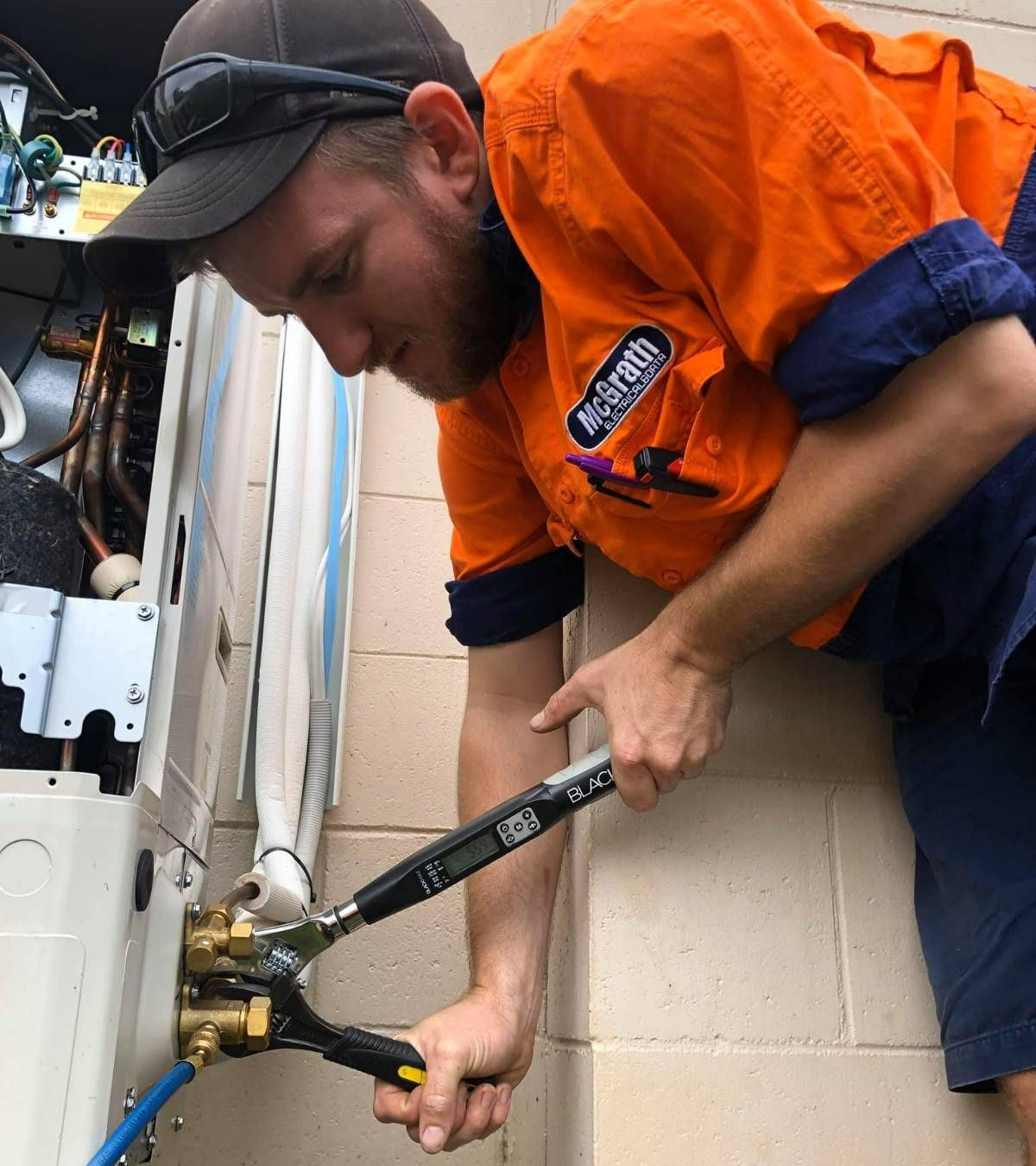 A Mechanic in Orange Shirt Uses Torque Wrench on an Air Conditioner Unit — McGrath Electrical & Data in South Grafton, NSW