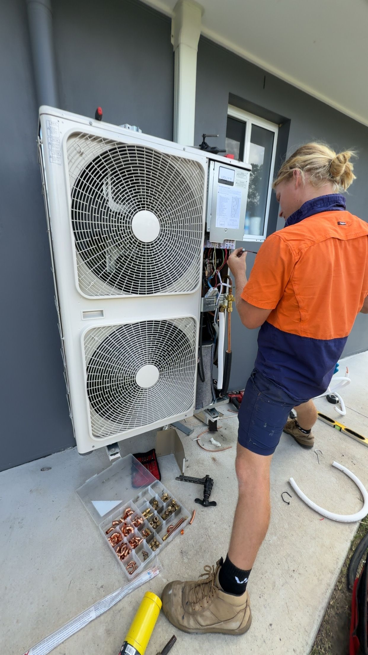 A electrician is installing an Air Conditioning Unit Mounted on a Wall  — McGrath Electrical & Data in Yamba, NSW
