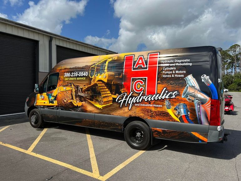 Black AC Hydraulics van with truck graphic parked outside a warehouse under cloudy skies
