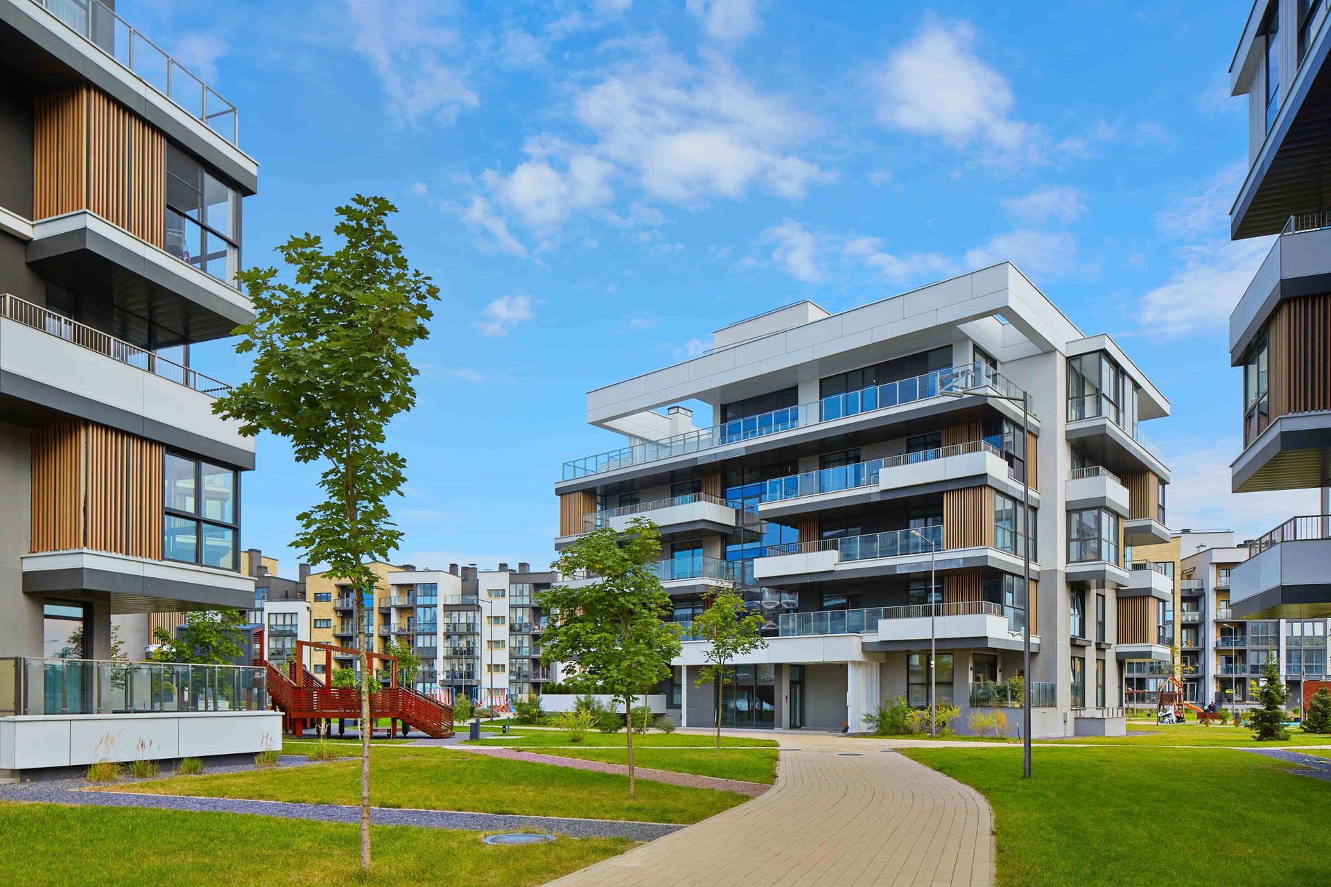 Modern apartment complex with balconies, green courtyard, and curved walkway under a blue sky