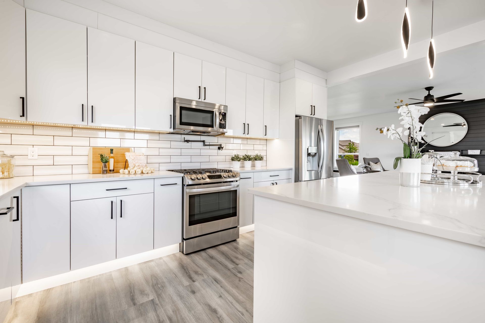Bright modern white kitchen with stainless steel appliances, island, and light wood flooring