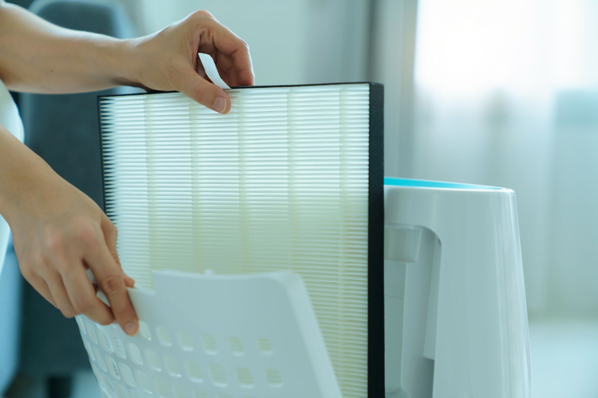Hands replacing a white air purifier filter beside a white unit