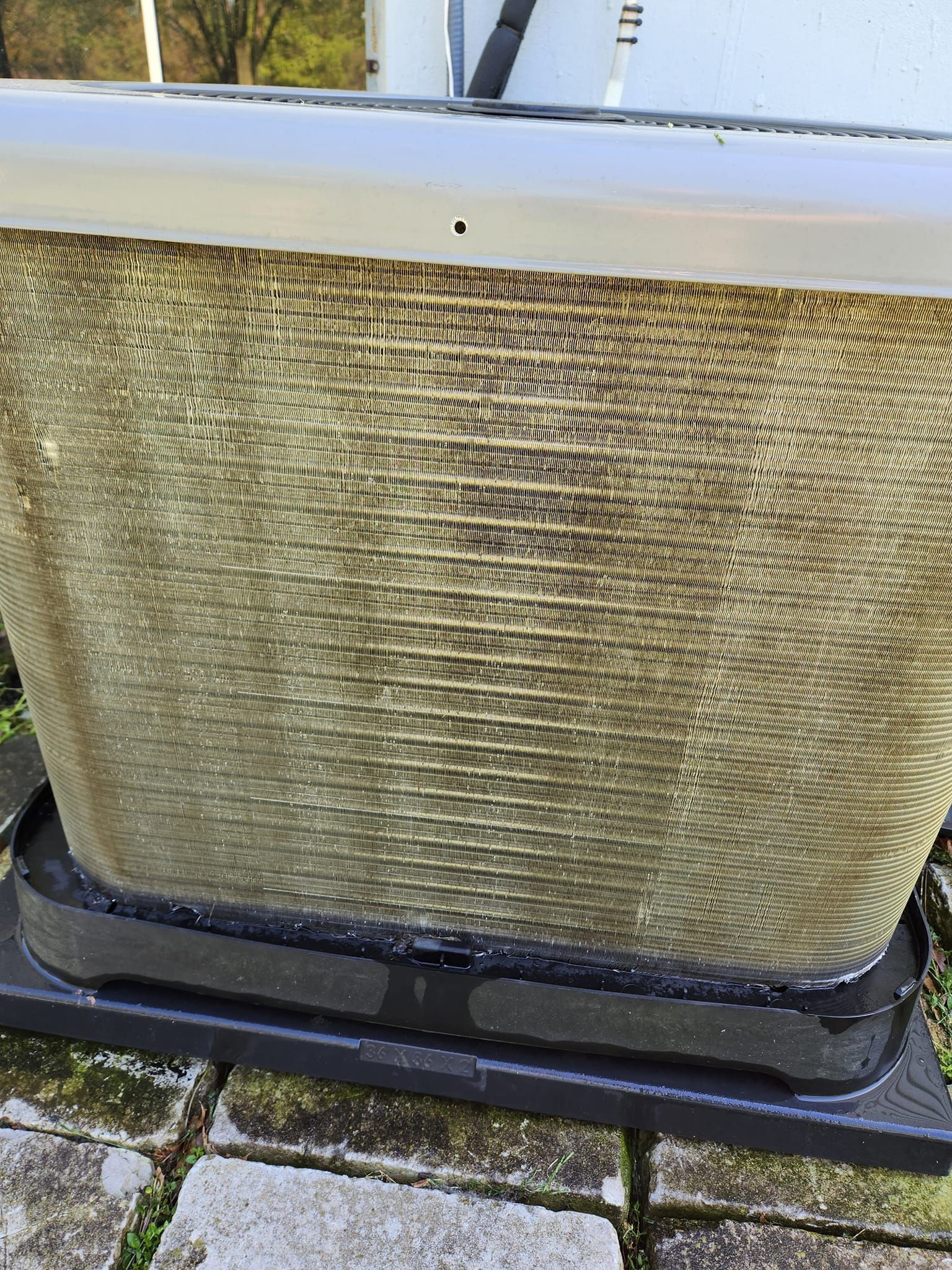 Large beige woven outdoor patio basket on a black base, sitting on a stone surface with grass around it