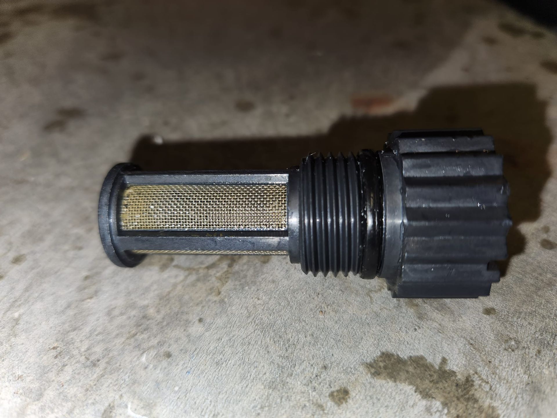 Black threaded plastic cap with mesh filter on a concrete floor