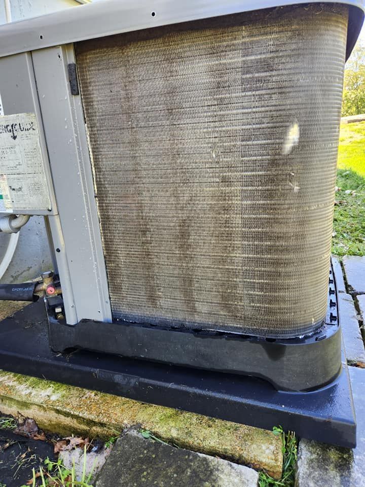 Dirty outdoor HVAC condenser unit with a stained metal coil and mossy base, near a walkway