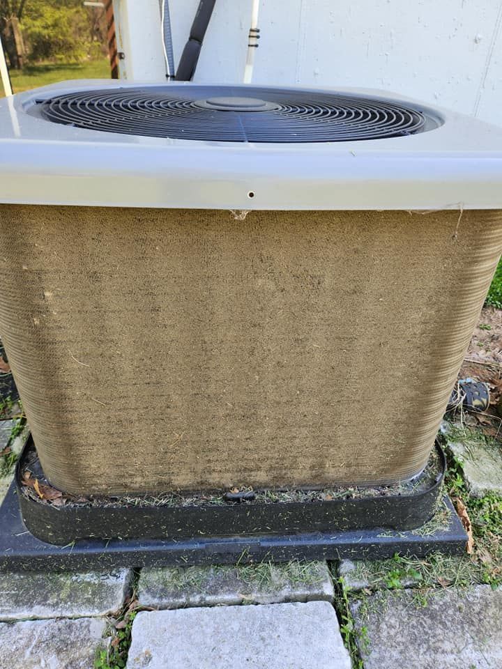 Outdoor air conditioner unit with a beige grille and black fan on top, sitting on a concrete base.