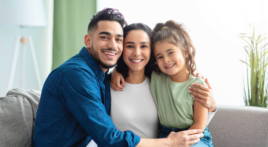 Smiling family sitting on a couch, hugging in a bright living room.