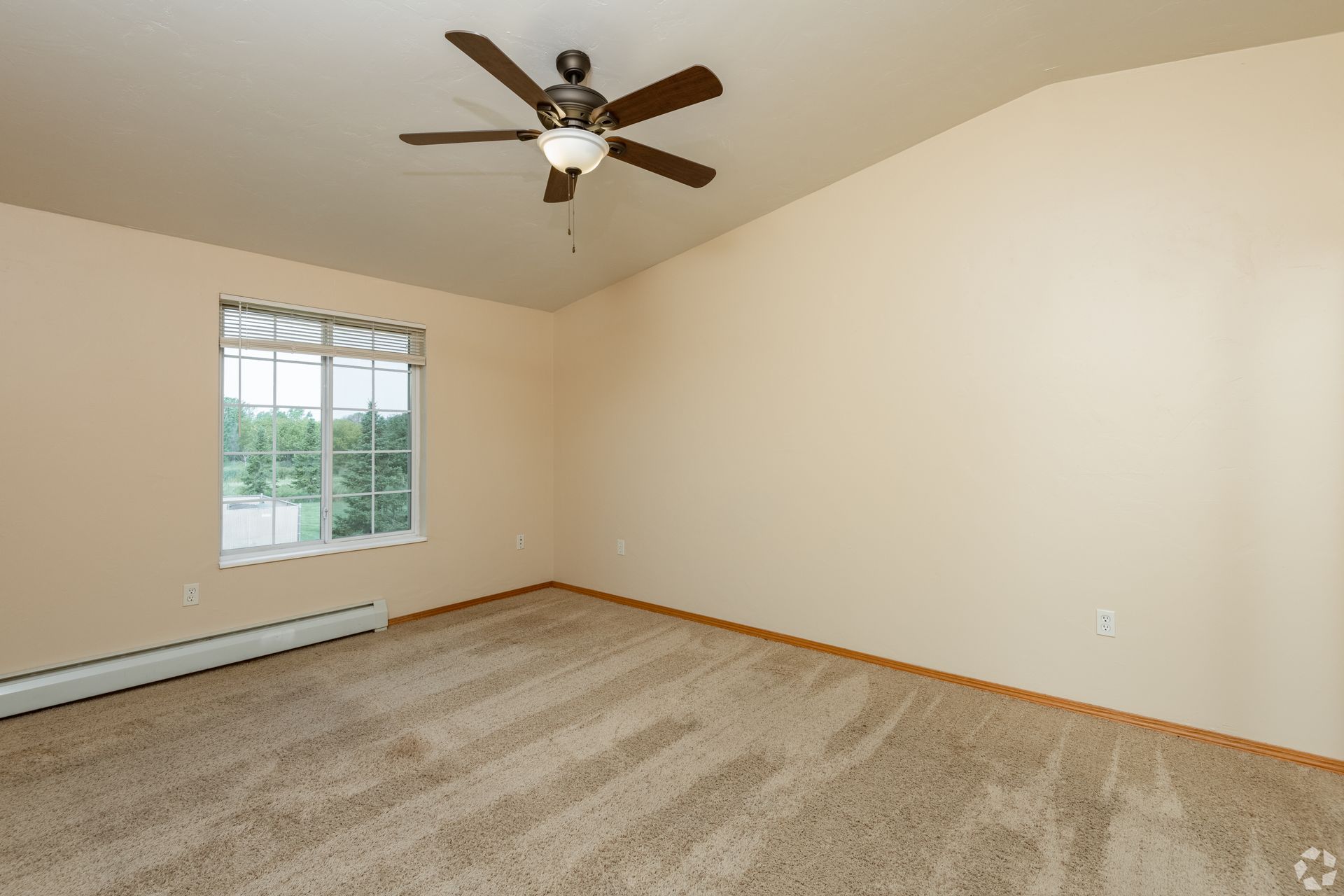 Empty beige bedroom with carpet, ceiling fan, and a window with blinds