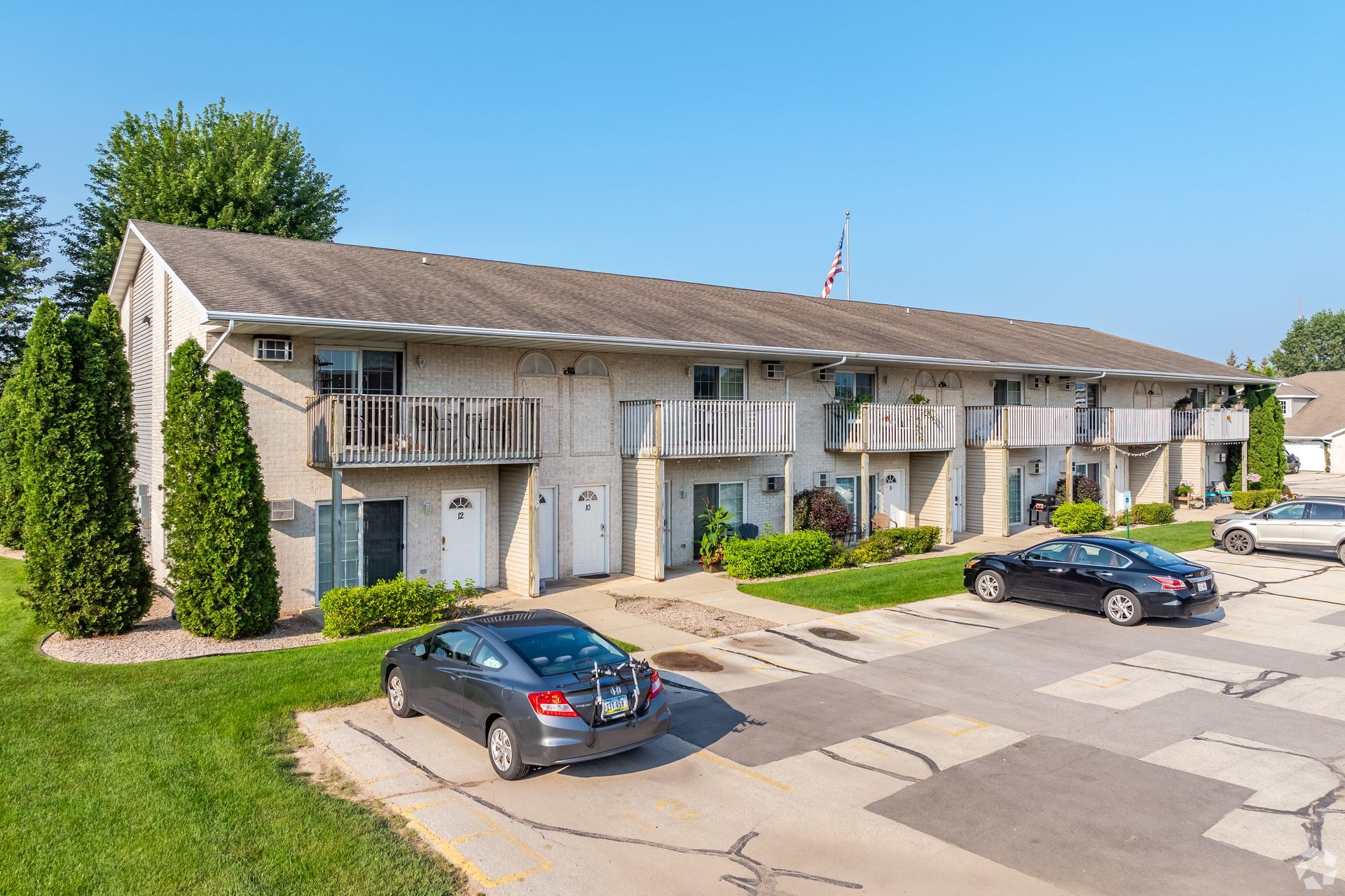 Apartment building with balconies and parked cars in a sunny residential lot