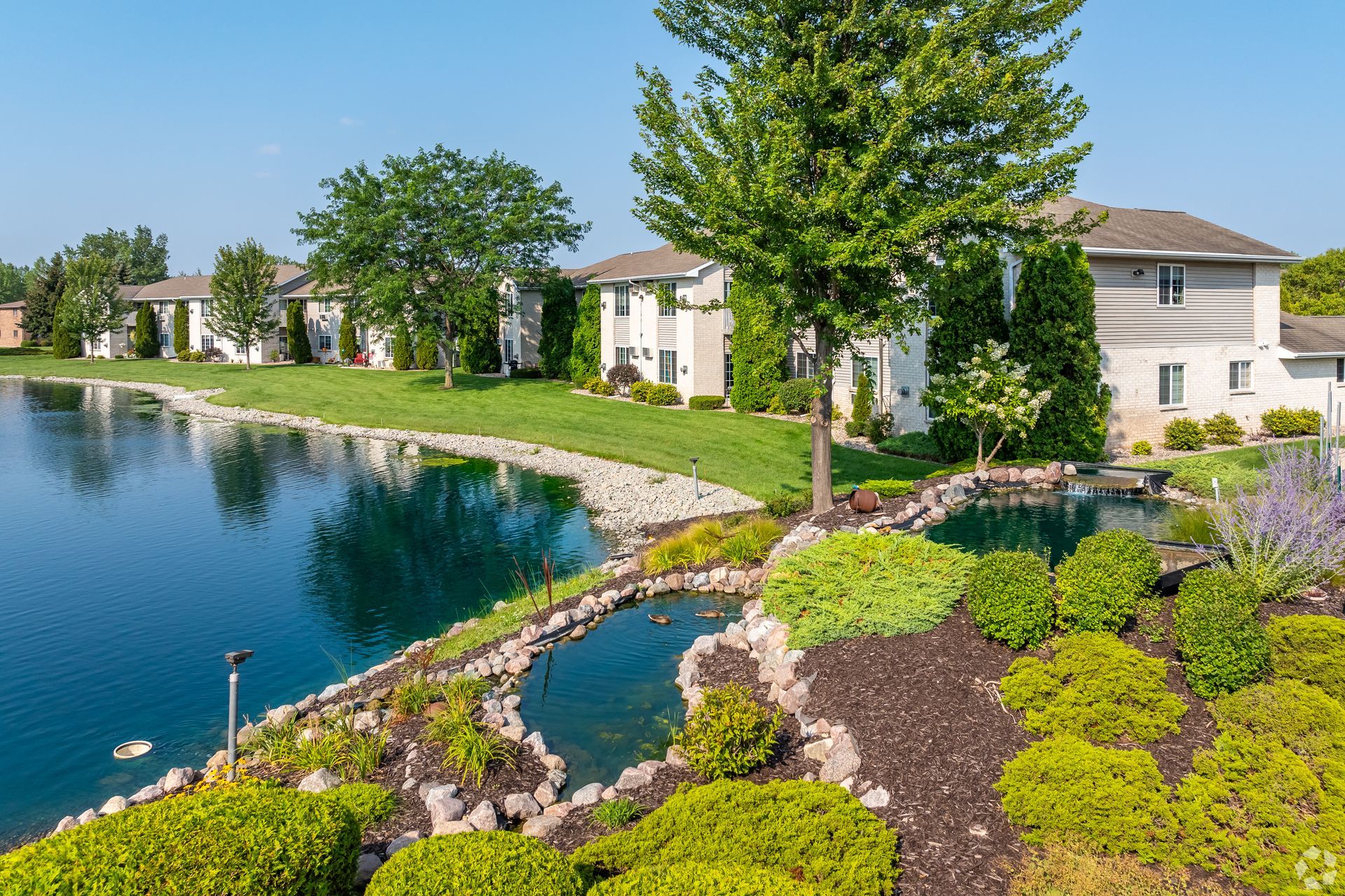 Landscaped lakeside apartments with green shrubs and trees on a sunny day