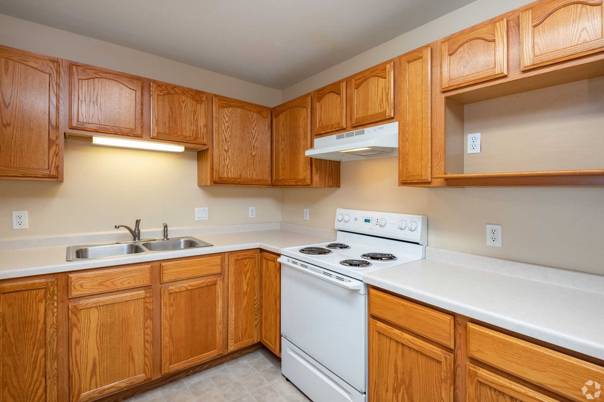 Small kitchen with oak cabinets, white appliances, beige countertops, and a double sink.