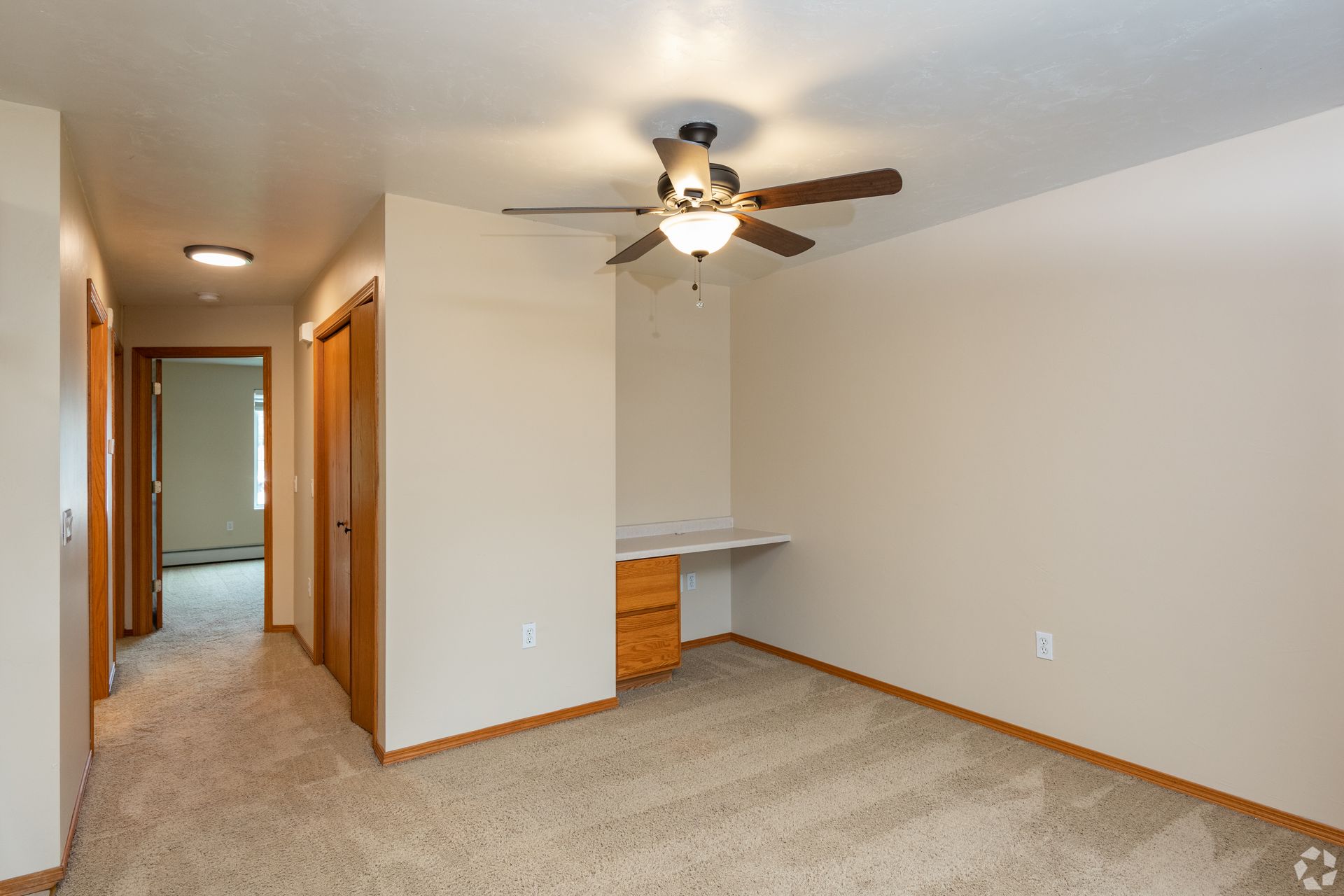 Empty carpeted bedroom with ceiling fan, open closet nook, and hallway doorway