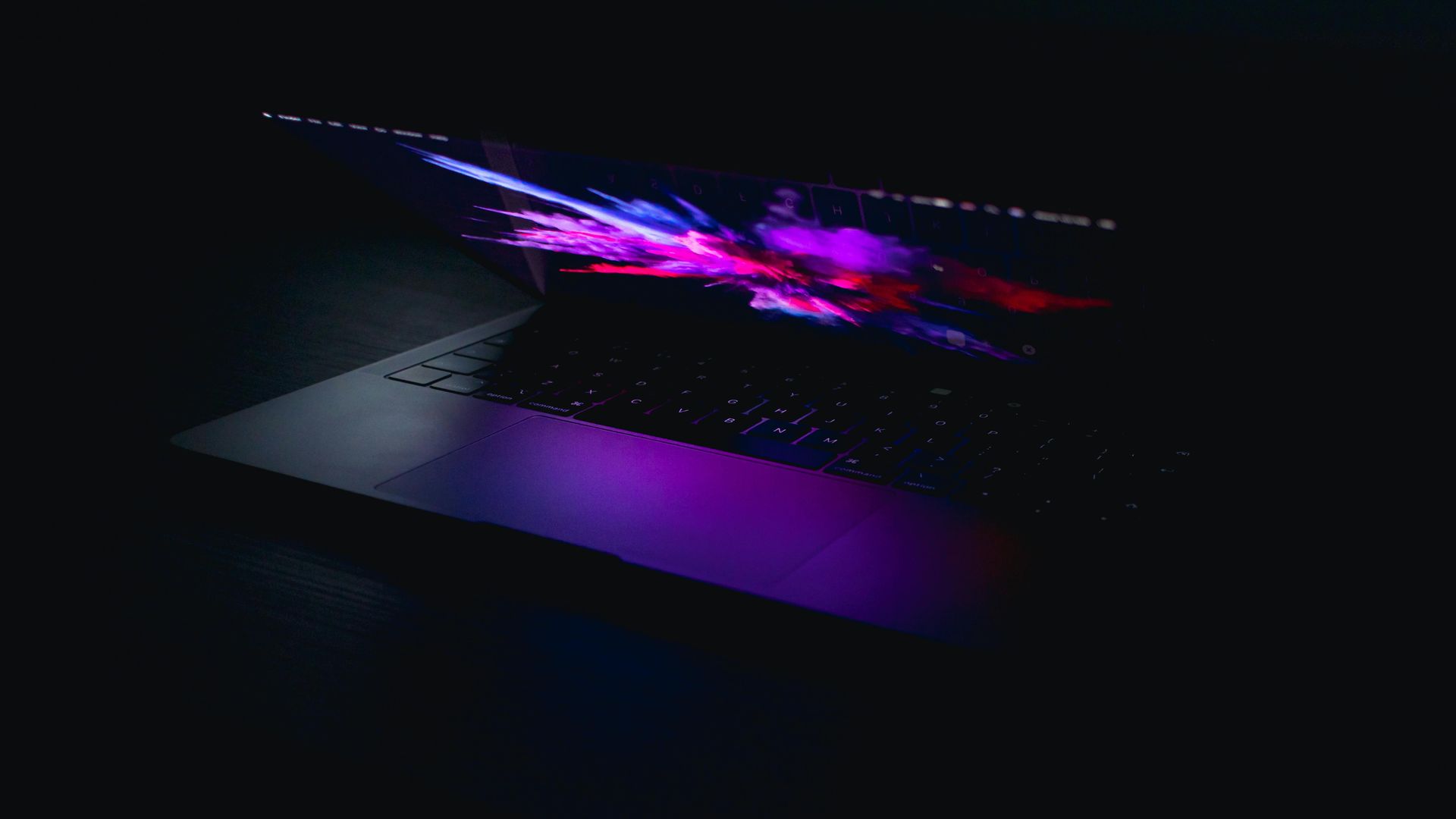 Laptop with a colorful, abstract display, emitting purple and blue light in a dark setting.