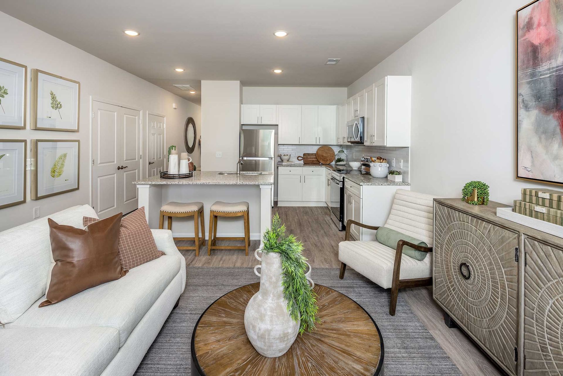 Bright, modern living room with white sofa, woven chairs, round coffee table, and open kitchen.
