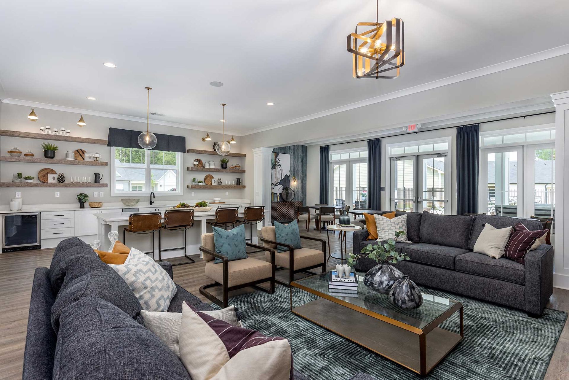 Modern open living room with gray sofas, teal chairs, a glass coffee table, and bright kitchen shelves