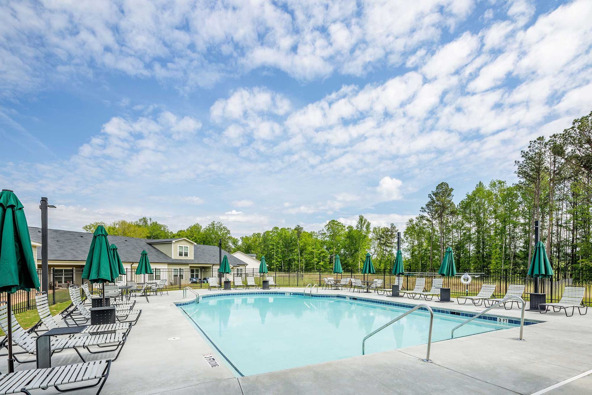 Outdoor swimming pool with lounge chairs and green umbrellas under a bright, cloudy sky