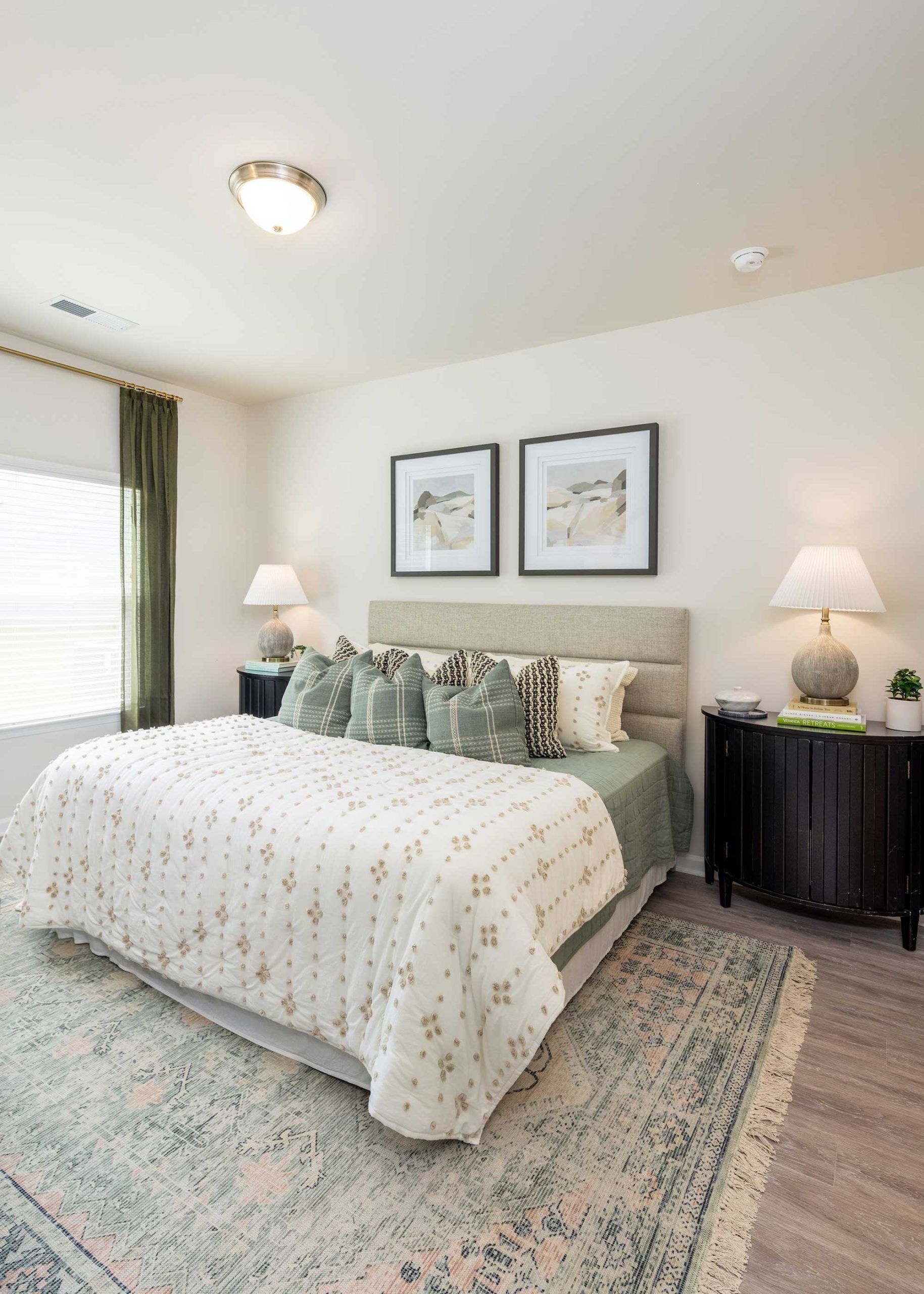 Bright bedroom with a bed, patterned rug, framed art, and a bedside lamp
