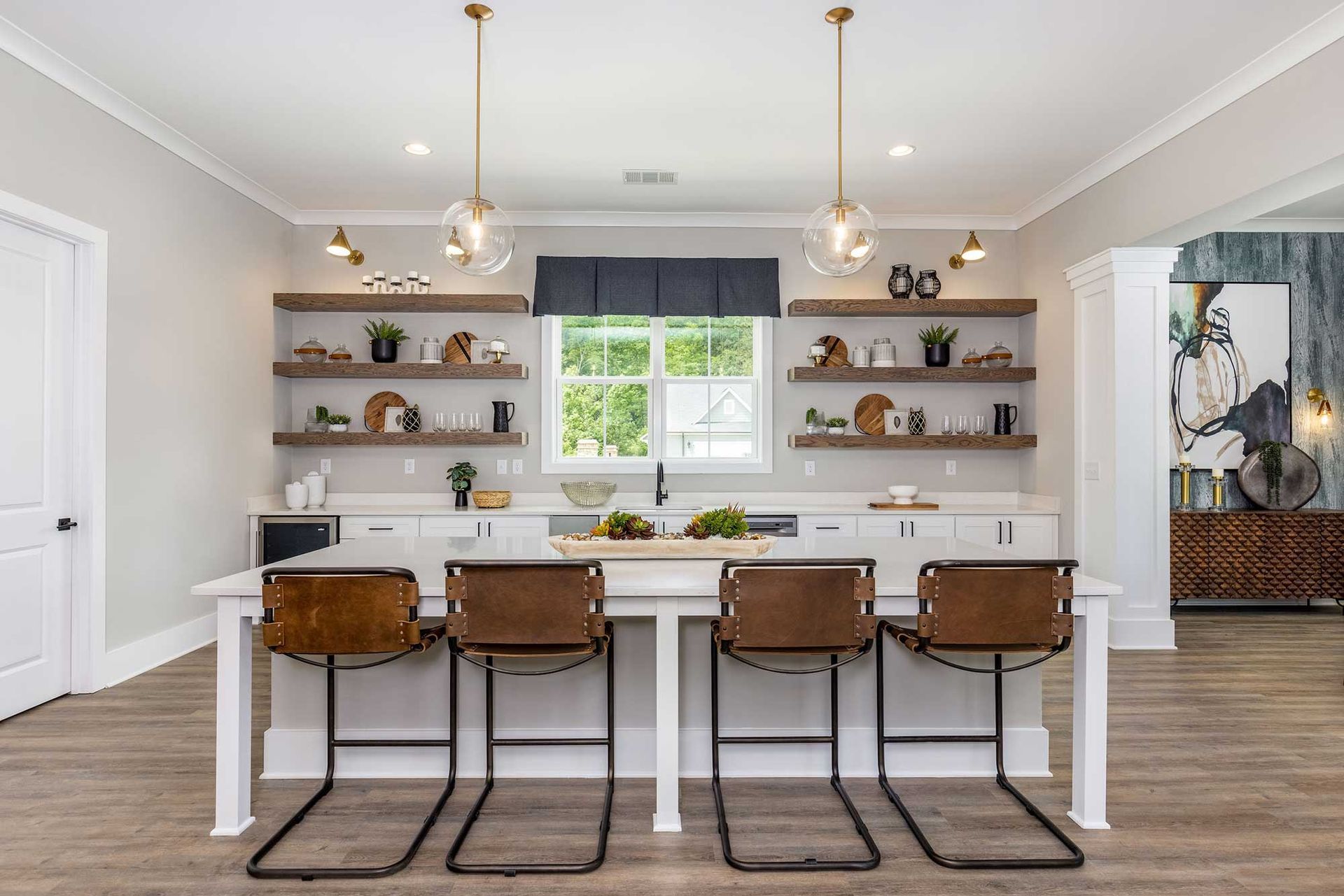 Bright modern kitchen with white island, brown barstools, open shelves, and a window over the sink