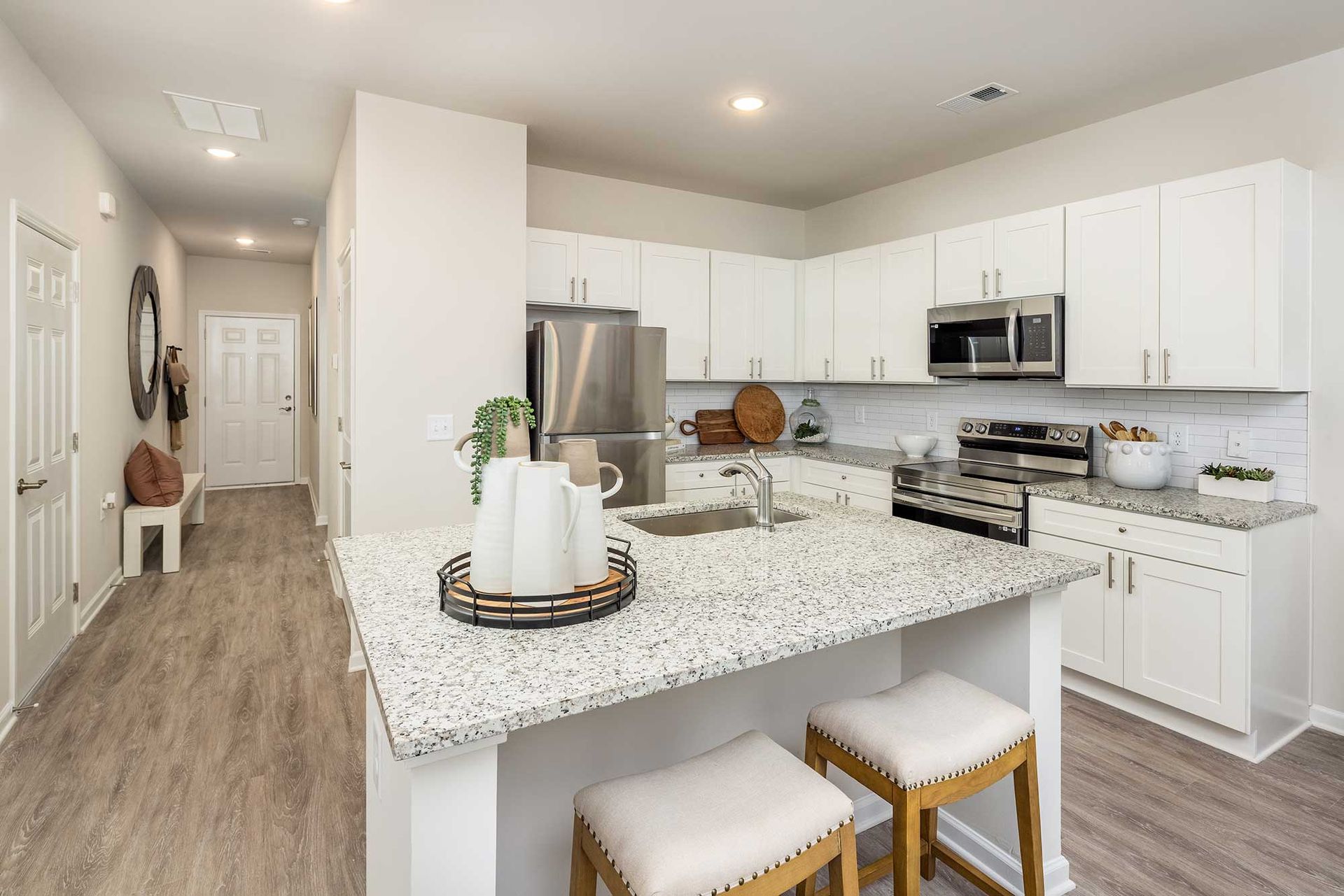 Modern white kitchen with large island, granite countertops, bar stools, and stainless steel appliances