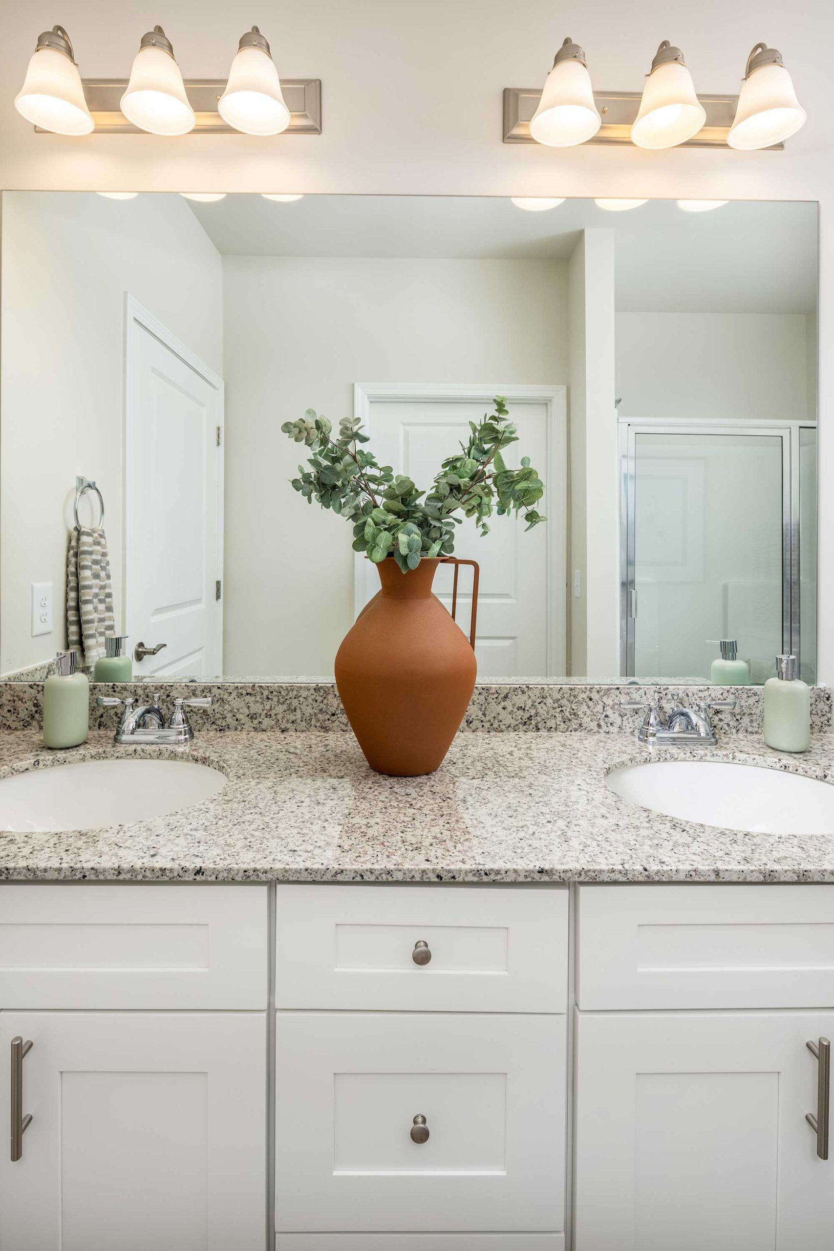 Bathroom vanity with speckled countertop, terracotta vase, and a large mirror under warm lights
