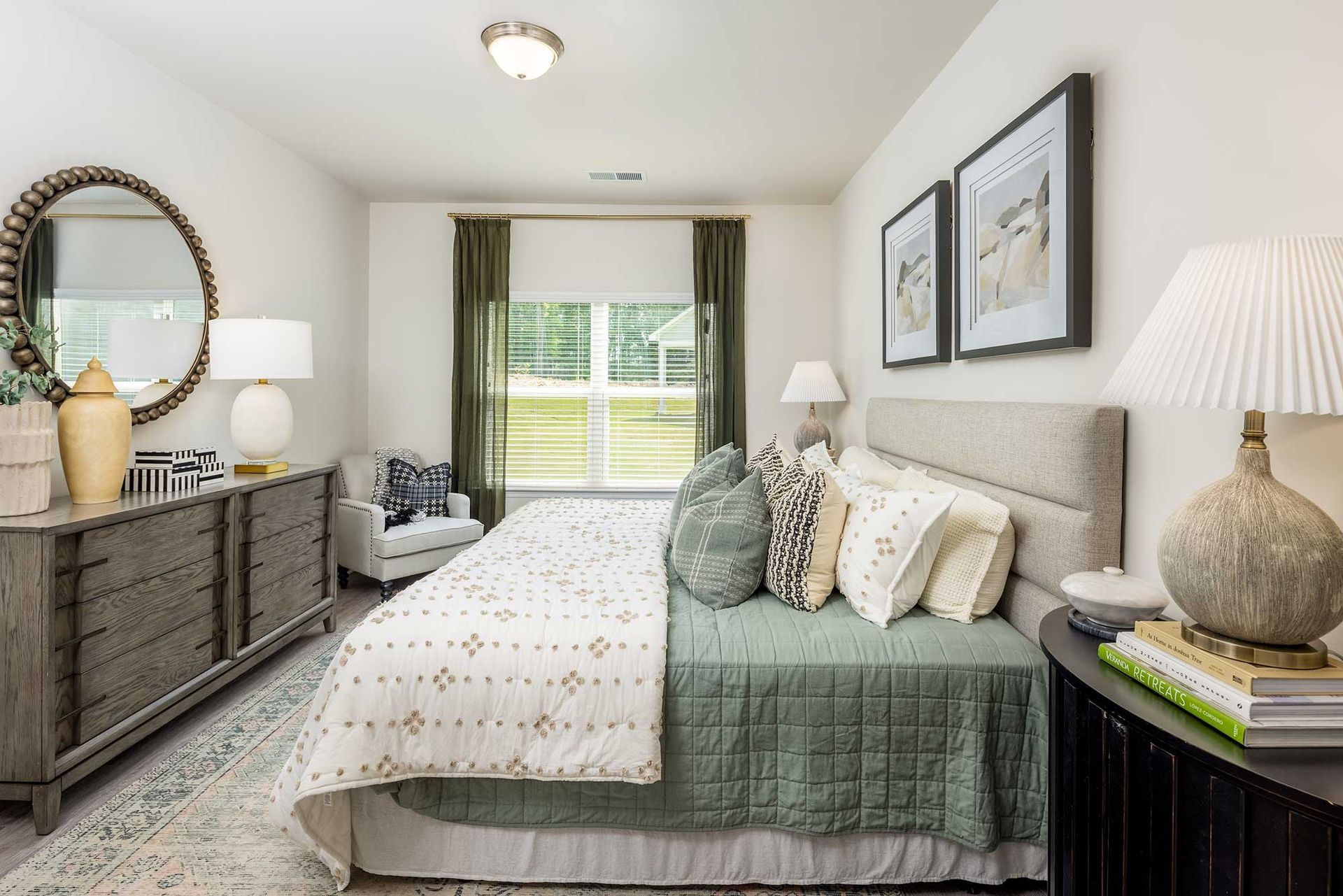 Bright bedroom with a bed, dresser, lamps, and window with green curtains and a view outside