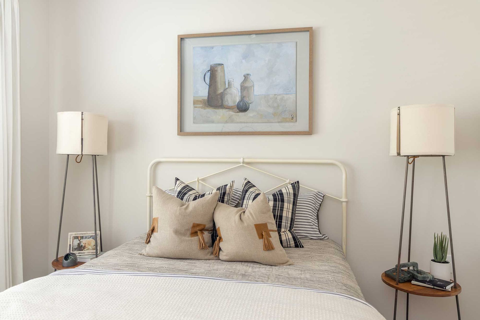 Cozy bedroom with a neatly made bed, neutral decor, bedside lamps, and framed art above the headboard