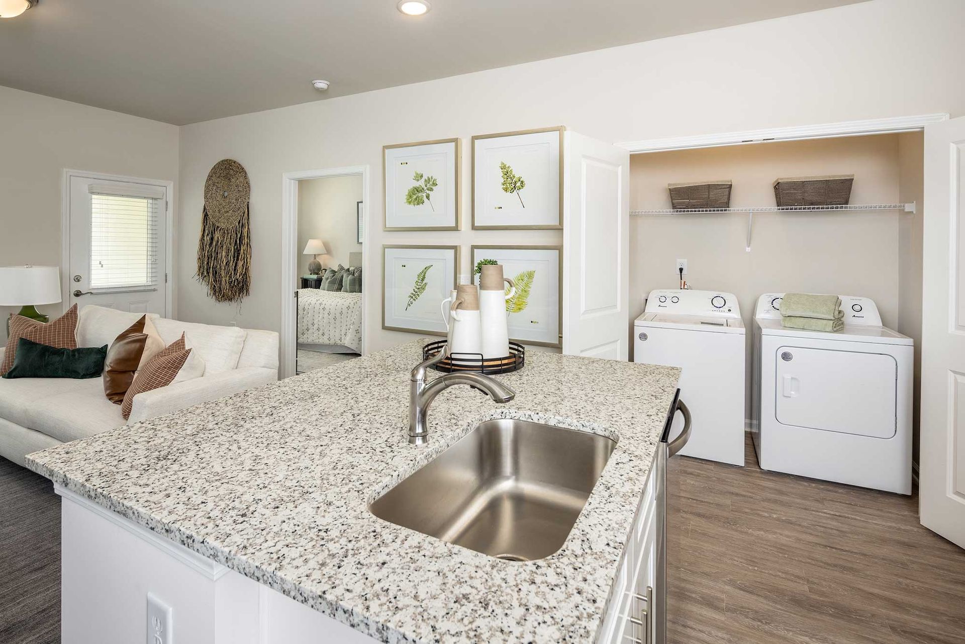 Bright modern kitchen with granite island, stainless sink, white washer and dryer, and living area beyond