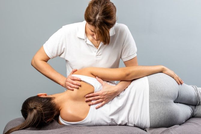 Therapist performing a shoulder massage on a client lying on a treatment table