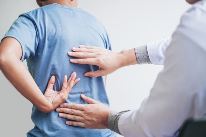 Doctor examining a patient's back with hands, suggesting physical therapy or medical assessment