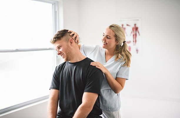 Woman giving man a shoulder massage in a bright clinic room
