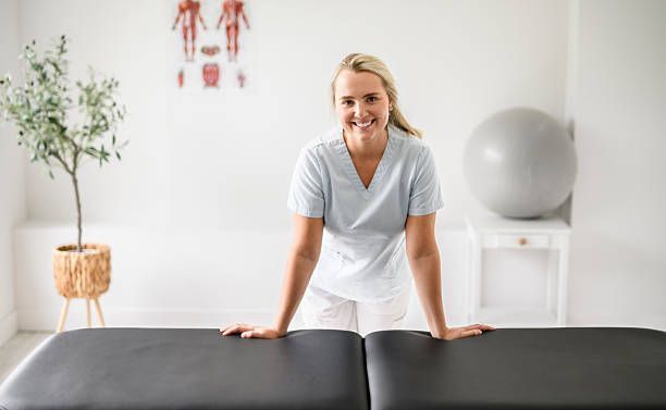 Woman smiling behind a black massage table in a bright therapy room