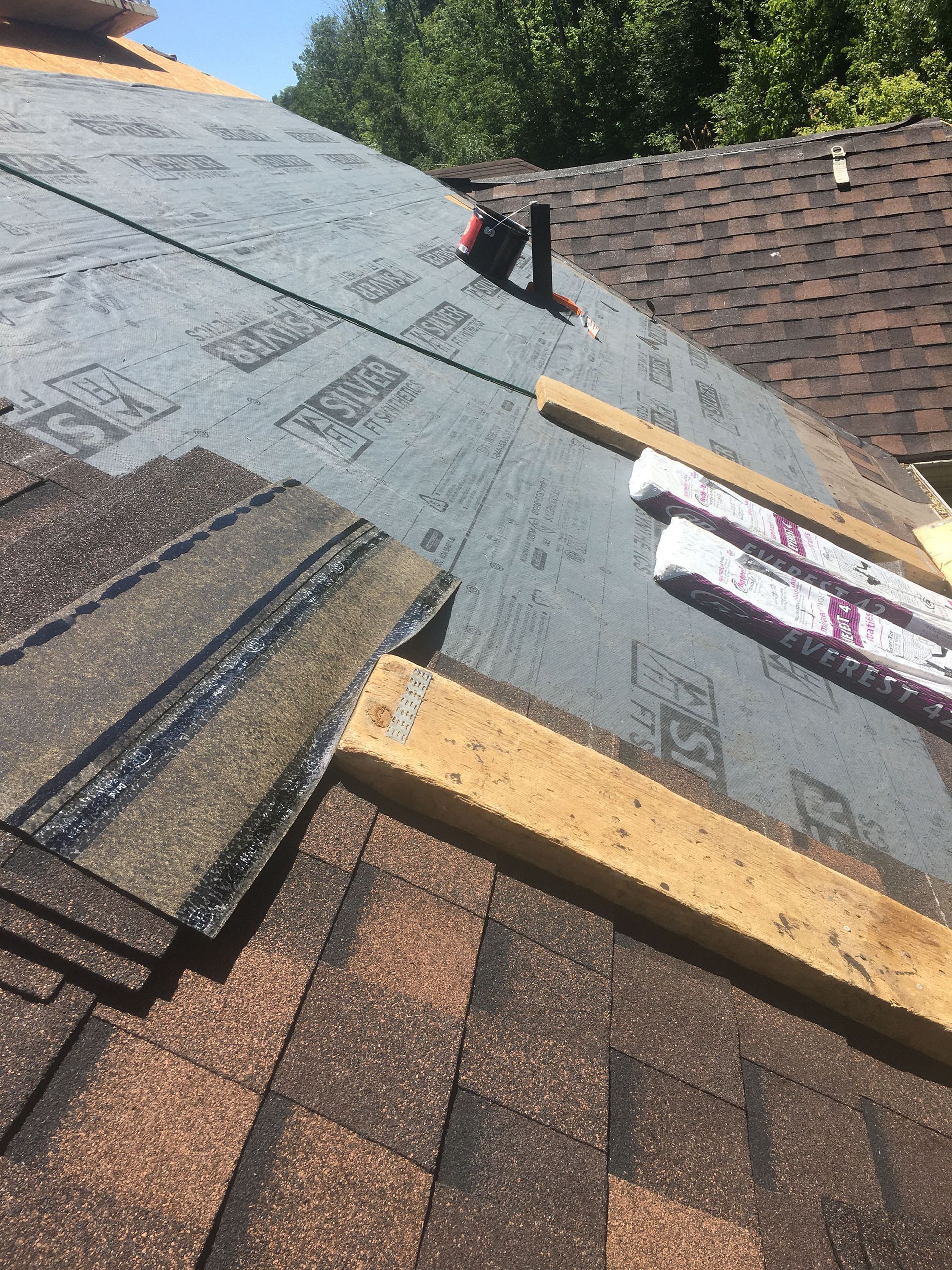 Un toit en construction avec de nouveaux bardeaux, une sous-couche grise, un évent de plomberie et des planches de bois pour l'échafaudage.