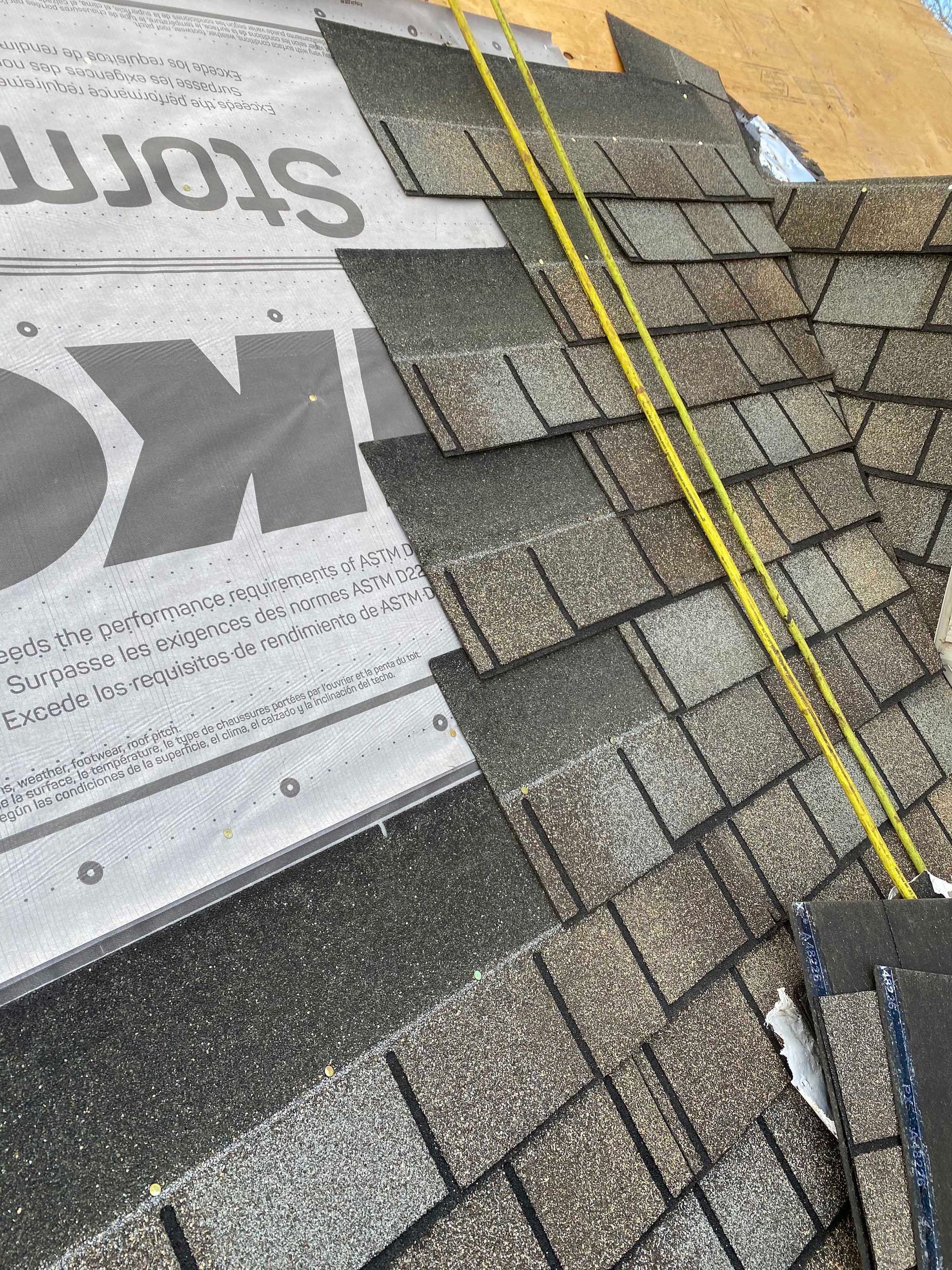 Toiture partiellement recouverte de bardeaux en construction, avec des bardeaux d'asphalte gris posés sur une sous-couche synthétique blanche.
